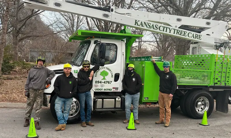 Five tree care crew members with hard hats pose by their company's green and white boom truck