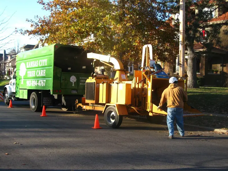 Kansas City Tree Care crew operating a wood chipper with a green truck on a residential street