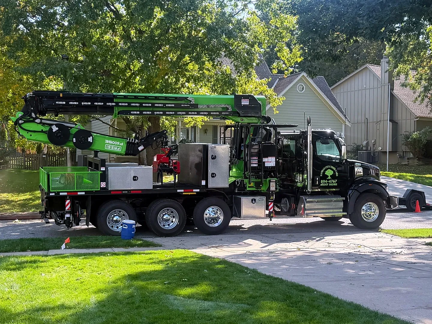 Black Kansas City Tree Care crane truck with a lime-green boom parked on a residential street