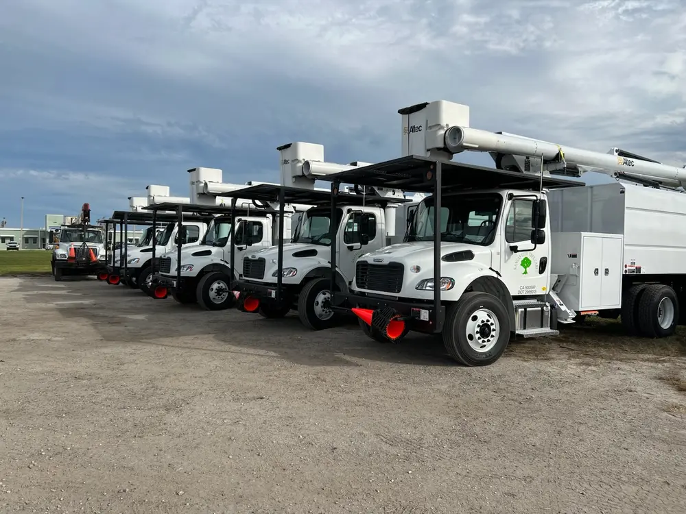 Row of white Kansas City Tree Care bucket trucks parked in the yard
