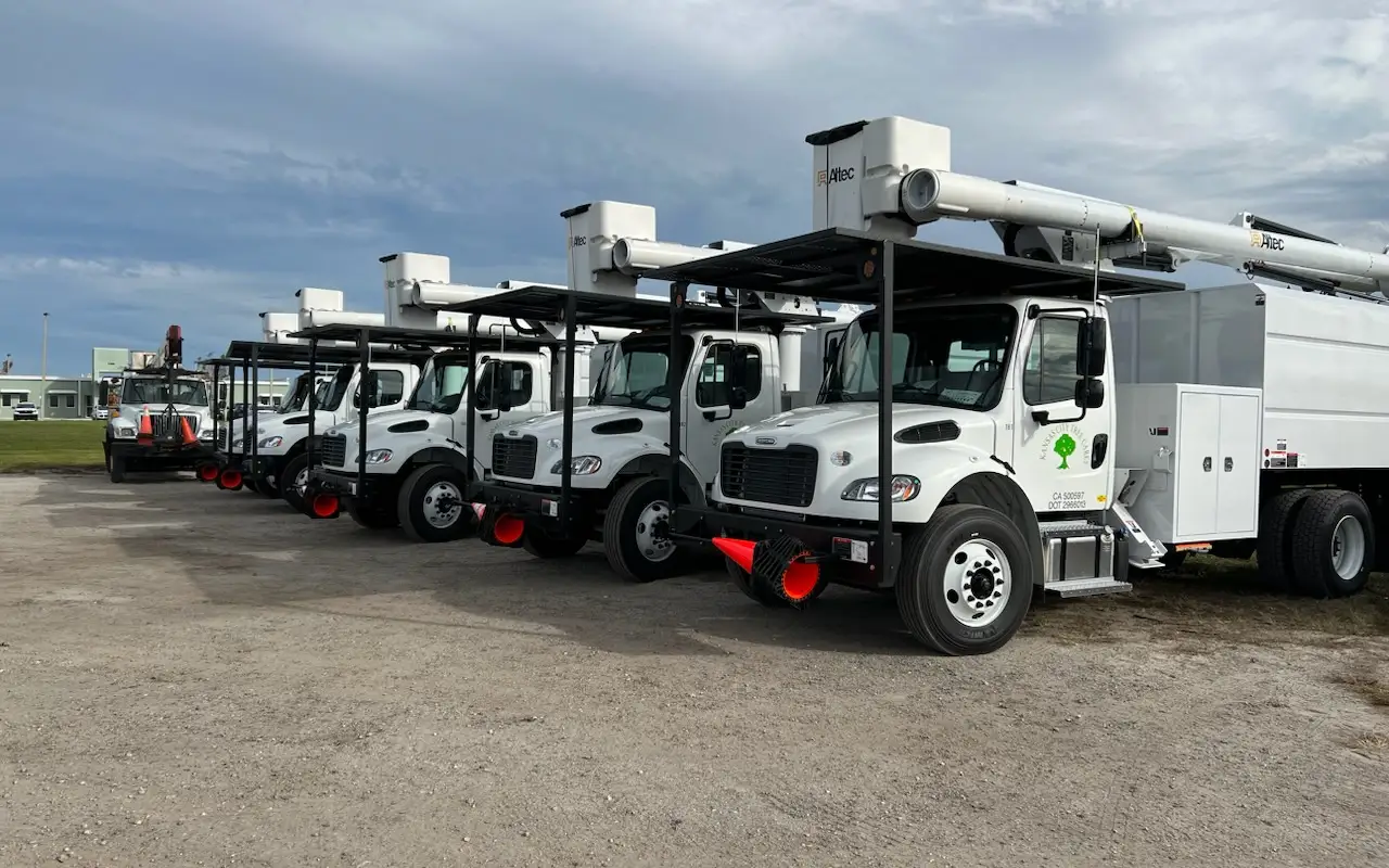 Row of white Kansas City Tree Care bucket trucks with their booms folded, parked in the yard